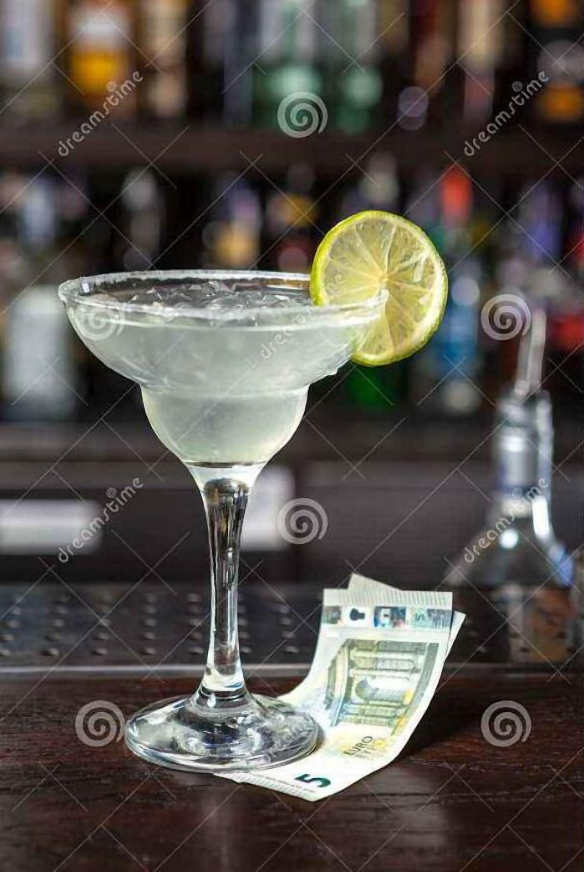 A martini glass with a lemon slice on a bar counter, next to a 5 Euro note.