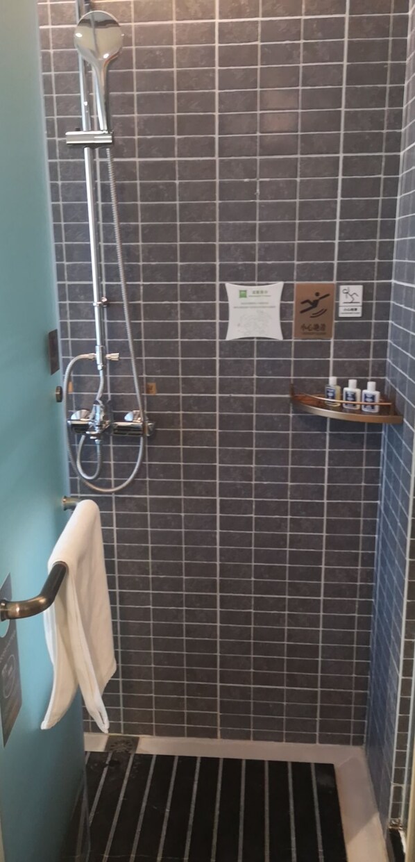 A shower area with a tiled wall, a handheld showerhead, a wall-mounted faucet, a towel rack, and a shelf with toiletries.
