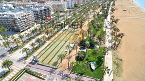 Vista aèria d'una ciutat costanera amb una platja, un passeig marítim ple de palmeres i edificis moderns.
