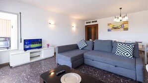 Un saló modern amb un sofà gris, una televisió de pantalla plana, una taula de centre i un quadre a la paret.