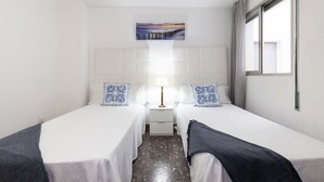 Habitació d'hotel amb dos llits individuals, una meseta de nit amb una làmpada, un quadre penjat sobre el llit i una finestra amb cortines.