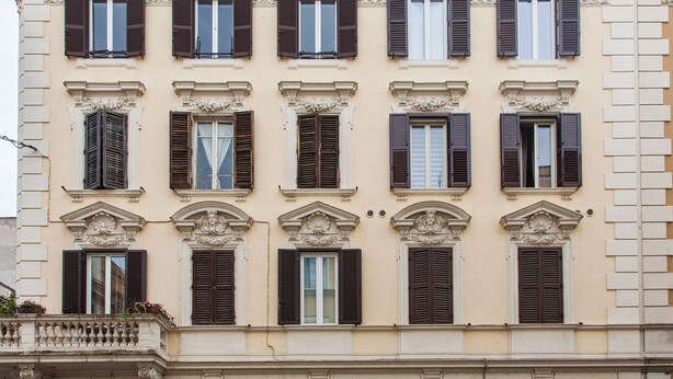 Eine Gebäudefassade mit zahlreichen Fenstern, jeweils mit Fensterläden, und dekorativen Stuckverzierungen.