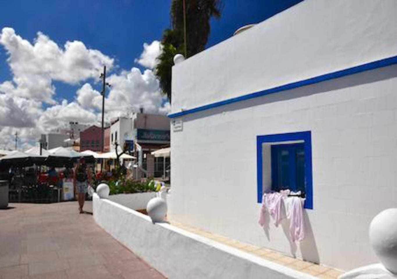 A white building with a blue door and a small window. There is a person walking on the sidewalk.