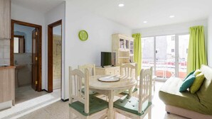 Uma sala de estar bem iluminada com uma mesa de jantar, cadeiras, um sofá e uma televisão.