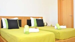 A hotel room with two beds, each with green bedding and a variety of pillows.