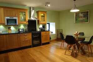 A modern kitchen with wooden cabinets, a stainless steel range hood, and a dining area with a glass table and black chairs.