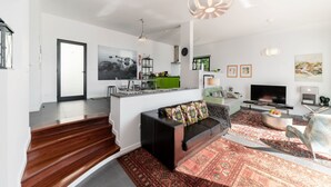 A modern living space with a staircase, a sofa, a TV, and a kitchen area.