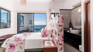 A bedroom with a bed, a nightstand, a lamp, a window with a view, and a bathroom with a sink and mirror.