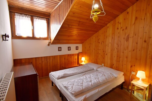 Una habitación con paneles de madera, una cama, dos lámparas de noche y un ventanal con cortinas.