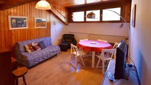Een gezellige kamer met houten wanden, een bank, een eettafel met stoelen, een televisie en een raam met uitzicht.