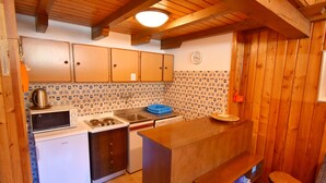 Een kleine keuken met houten kastjes, een magnetron, een fornuis en een spoelbak.