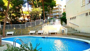 Ein Schwimmbecken mit Steinmauer, Bänken und einer Treppe, die zu einem Balkon führt.