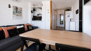 Eine moderne Küche mit weißen Schränken, einem Holztisch und einem grauen Sofa mit gemusterten Kissen.