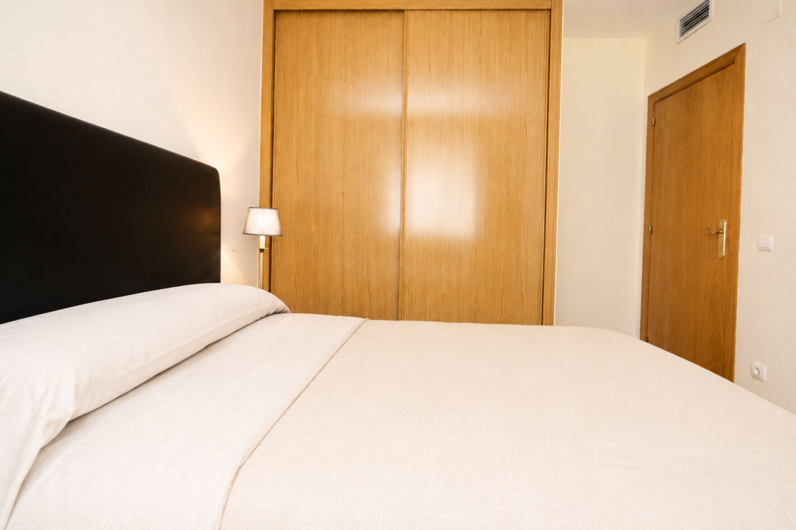 Un dormitorio con cama, armario de madera y mesita de noche con lámpara.