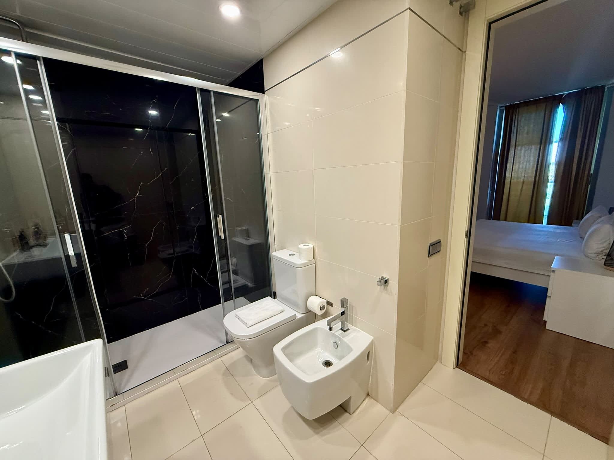 A modern bathroom with a glass shower enclosure, a toilet, a bidet, and a sink.