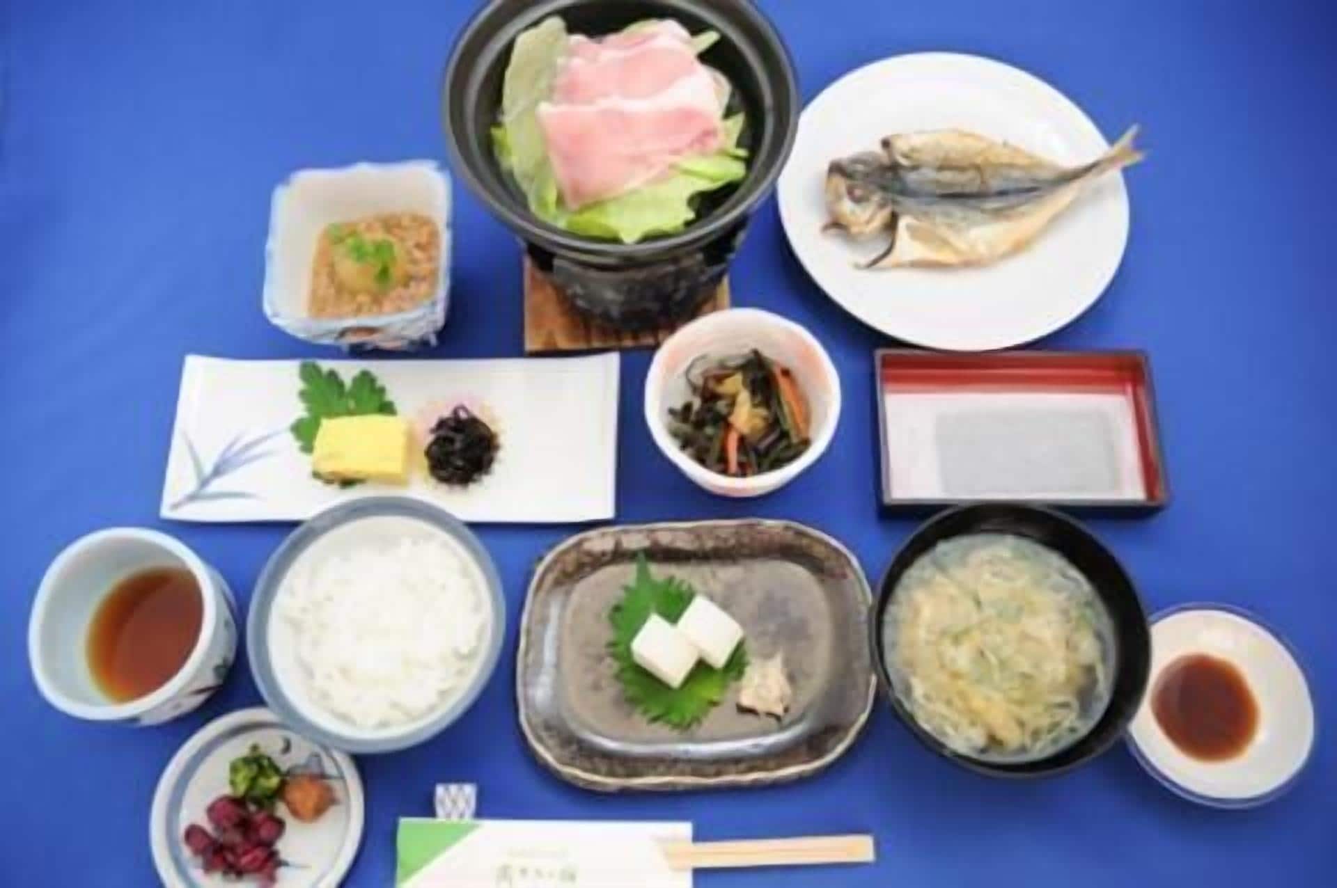 A variety of Japanese dishes including sushi, sashimi, and pickled vegetables arranged on a blue table.