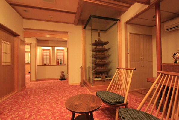 Une pièce de style japonais traditionnel, avec un sol recouvert de tatamis, une petite table en bois, un fauteuil rembourré et une cloison en verre ornée d’une maquette de pagode.