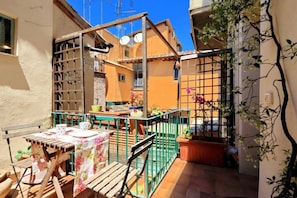 A small outdoor patio with a table and chairs, a green metal fence, and potted plants.