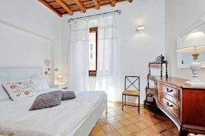 A bedroom with a bed, a chair, a dresser, a nightstand, and a window with curtains.