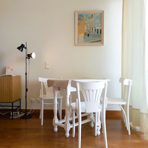 Una habitación con una mesa y sillas blancas, un cuadro en la pared y una lámpara de pie.