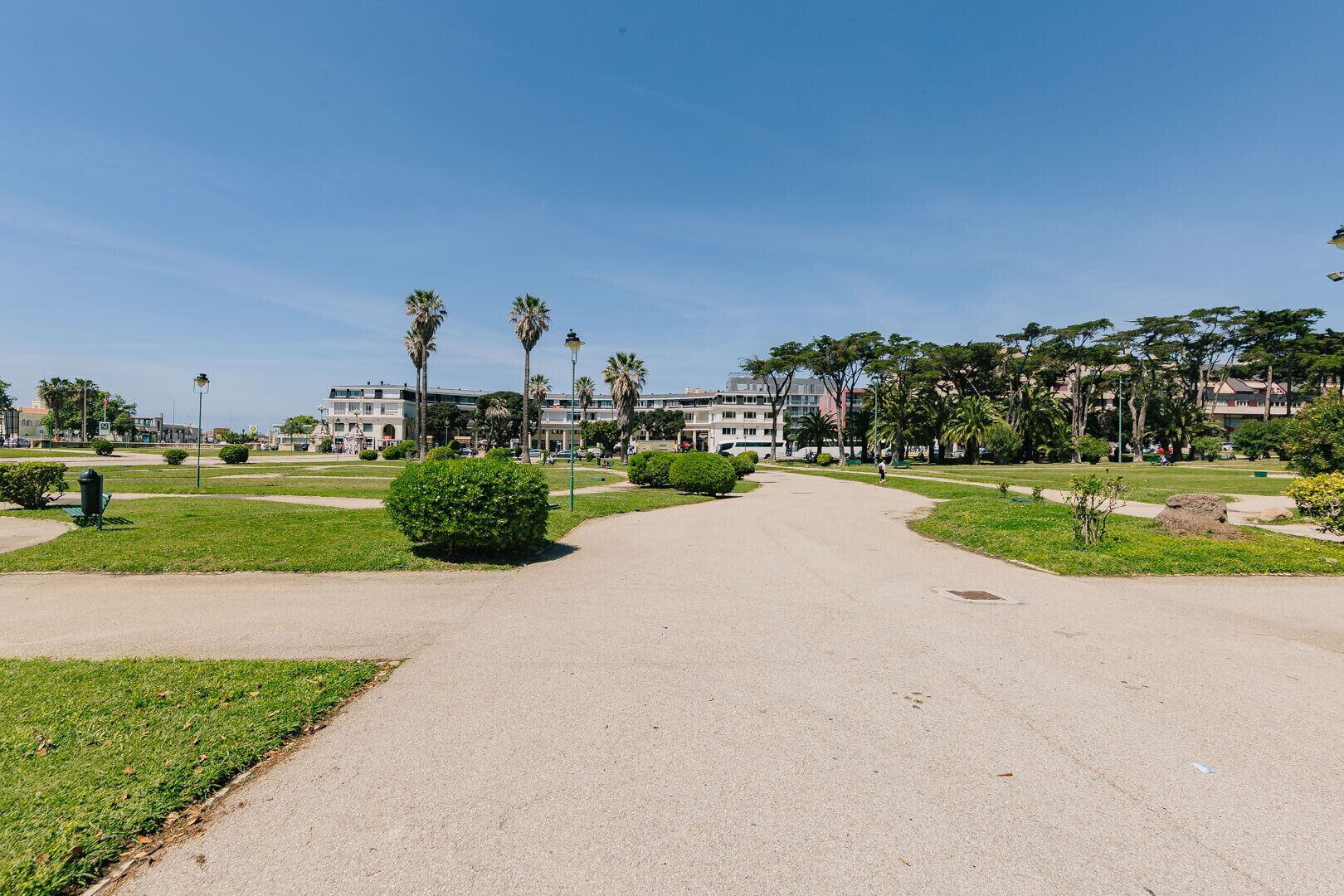 Ein gepflasterter Weg in einem Park mit grünem Rasen, Palmen und einem Gebäude im Hintergrund.