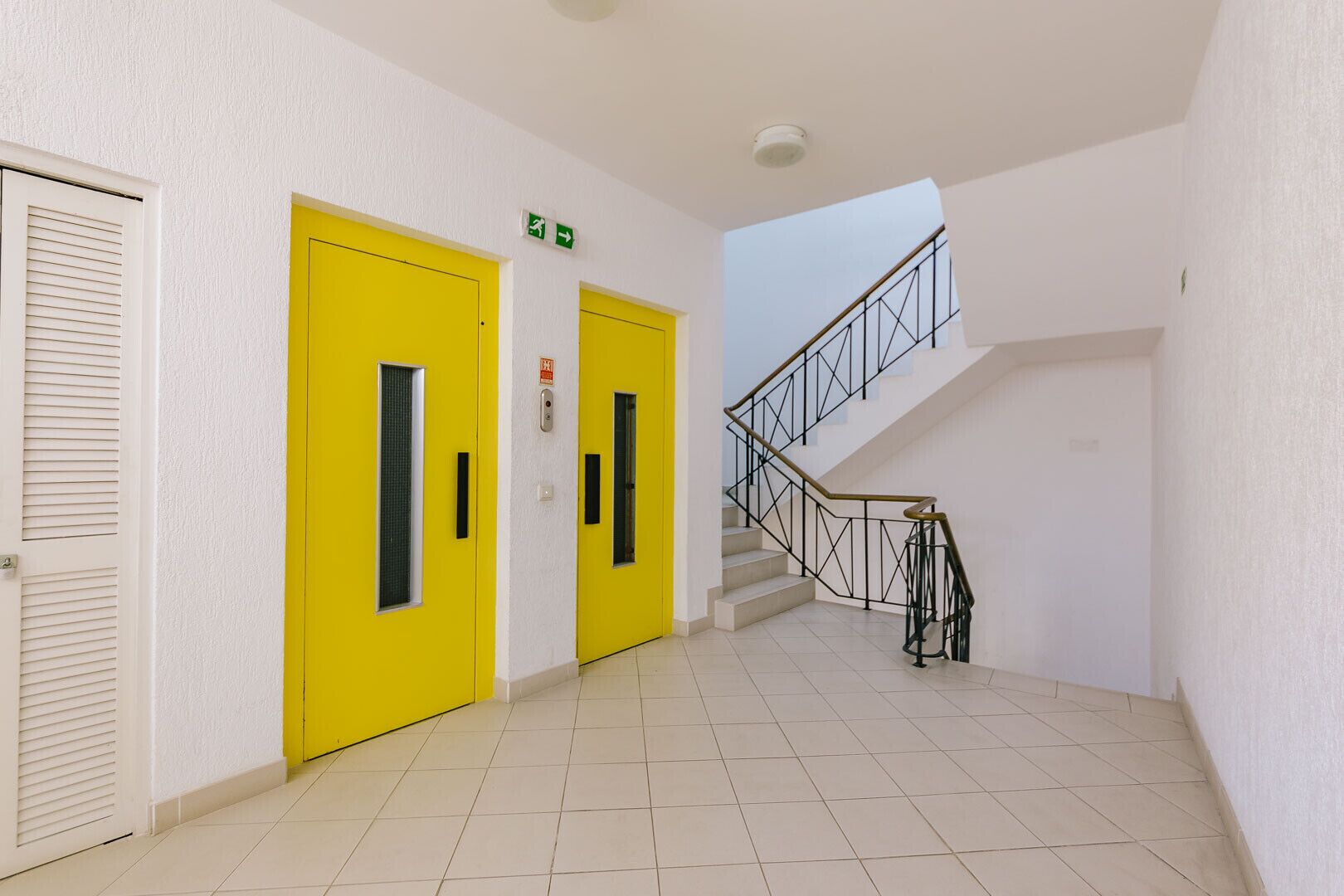 Ein Flur mit gelben Türen, einer Treppe und einem Rauchmelder.