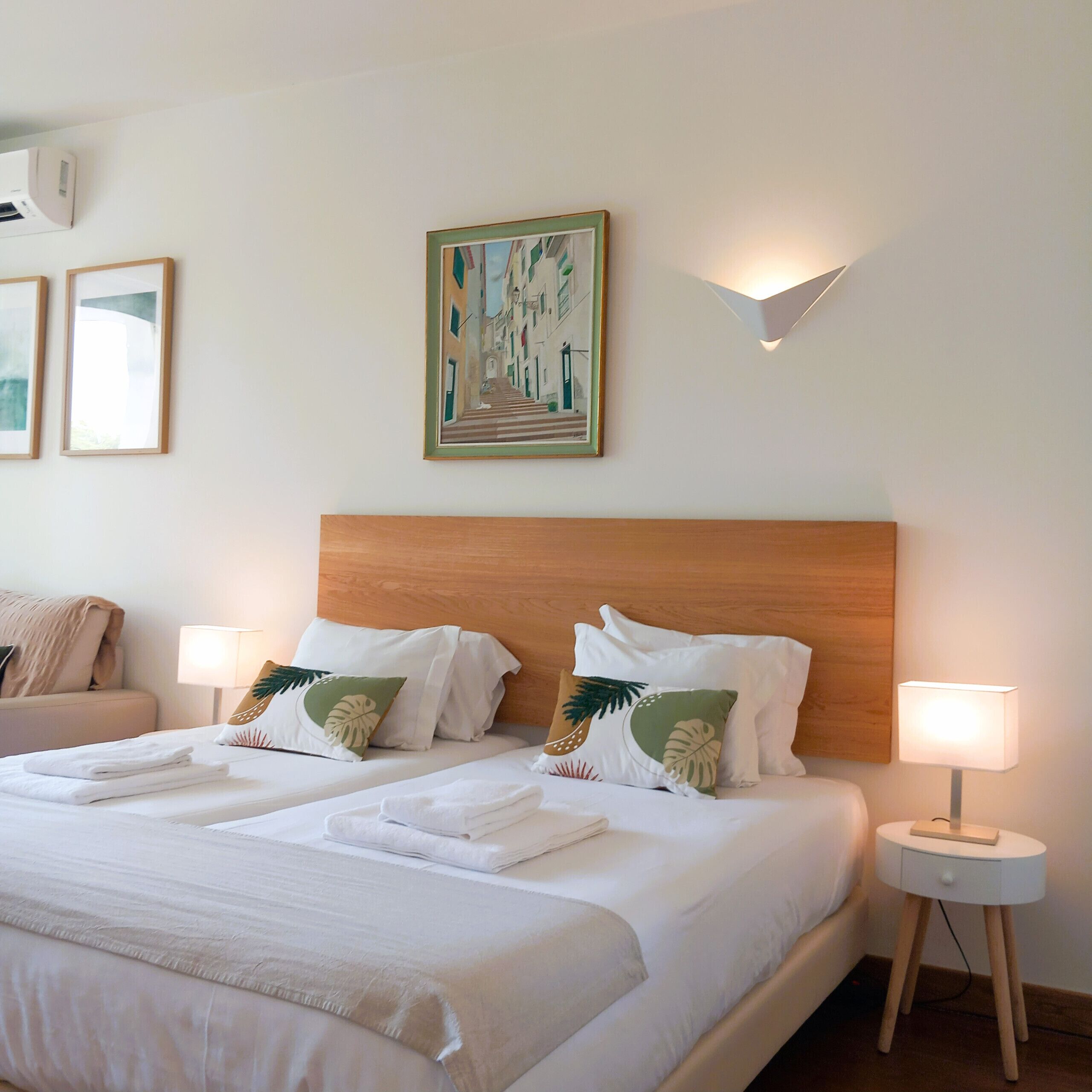Ein Hotelzimmer mit einem großen Bett, zwei Nachttischen mit Lampen, einer Kopfteil und einer Wandklimaanlage.