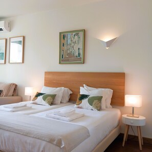 A hotel room with a large bed, two bedside tables with lamps, a headboard, and a wall-mounted air conditioner.