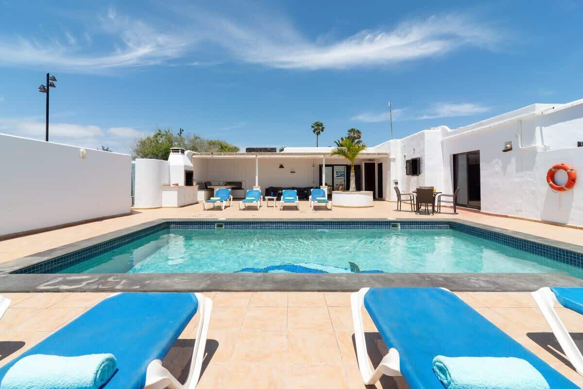 Una piscina con sillas de descanso, un área de estar techada y un flotador en la pared.