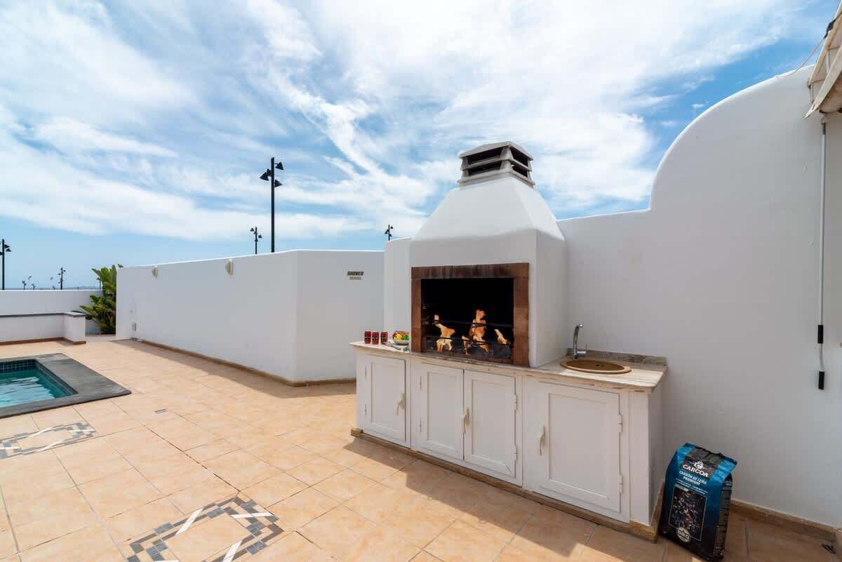 Un patio en la azotea con una barbacoa integrada, una piscina pequeña y piso de baldosas.