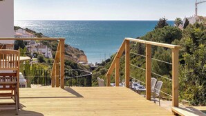 A wooden deck with a railing, overlooking a coastal area with buildings and a clear view of the sea. - Villa Diane, Luxury Cottage, Ocean views, pool (Benagil)