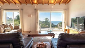 A living room with leather sofas, a coffee table, and a TV. Large windows offer a view of the sea and a cactus. - Villa Diane, Luxury Cottage, Ocean views, pool (Benagil)