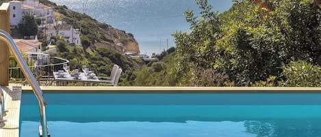 A swimming pool with a view of a coastal town and greenery.