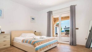 Ein Schlafzimmer mit Bett, Nachttisch, Kommode und Blick ins Freie.