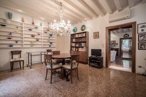 Un'area pranzo con un tavolo rotondo, sedie, un lampadario, mensole con oggetti decorativi, una libreria e una televisione.