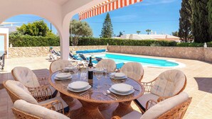 An outdoor dining area with wicker chairs, a round table, and a pool in the background.