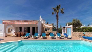 A swimming pool with lounge chairs, a building with a tiled roof, and palm trees.