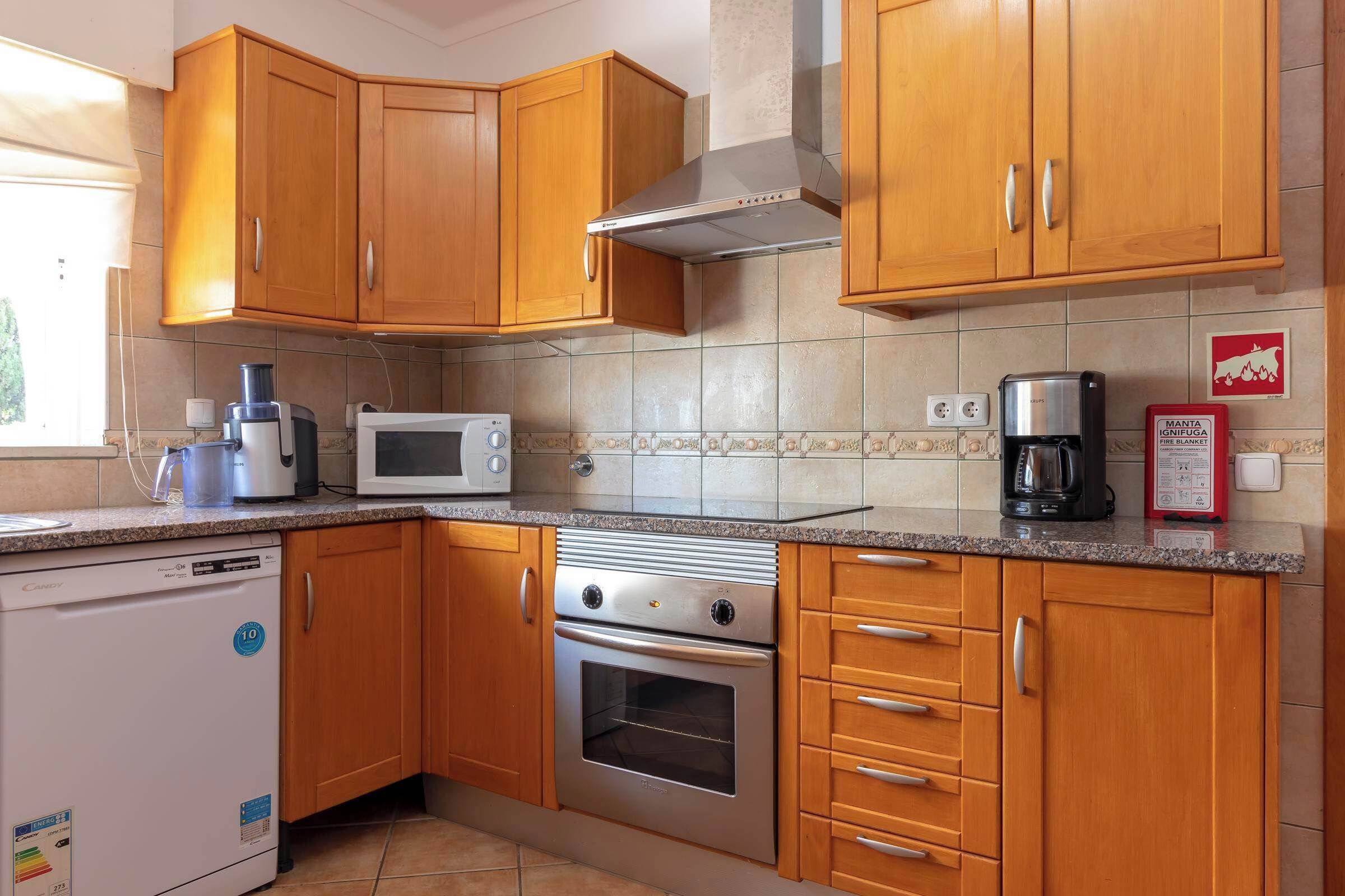 A kitchen with wooden cabinets, a stainless steel range hood, a microwave, a coffee maker, and a dishwasher.