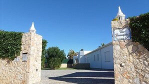 A stone gate with a sign reading 'Vila Bovedaida' leading to a building with a white facade and a stone wall.