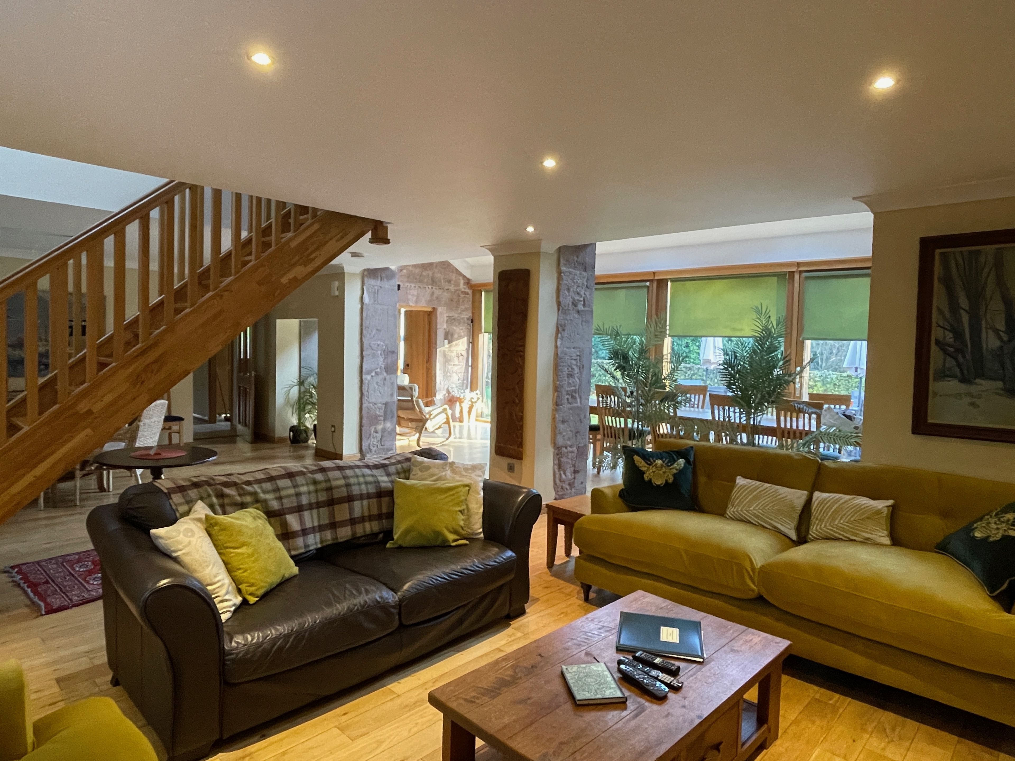 A living room with a brown leather sofa, a yellow sofa, a wooden coffee table, and a staircase.
