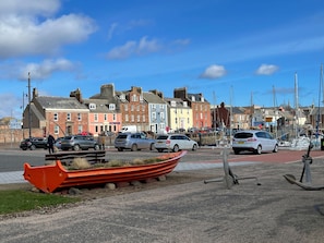 A coastal town with colorful buildings, a marina with boats, and parked cars along the street.