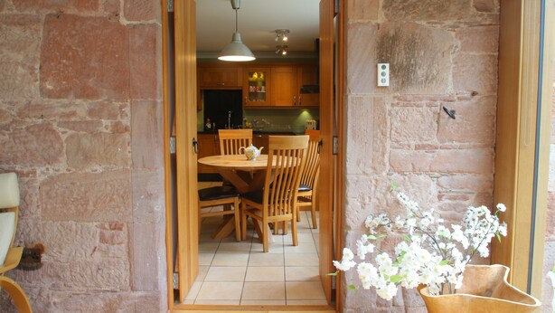 An open doorway leading to a dining area with wooden furniture and a stone wall.