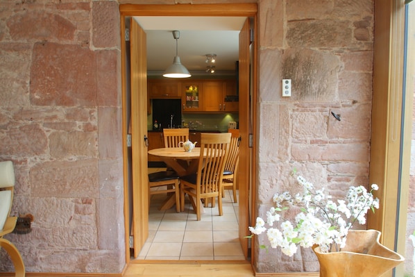 An open doorway leading to a dining area with wooden furniture and a stone wall.