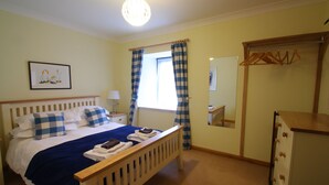 A bedroom with a bed, a bedside table, a dresser, a mirror, and a window with curtains.
