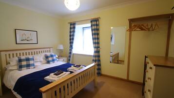 A bedroom with a bed, a bedside table, a dresser, a mirror, and a window with curtains.