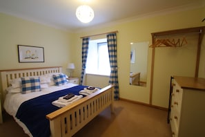 A bedroom with a bed, a bedside table, a dresser, a mirror, and a window with curtains.