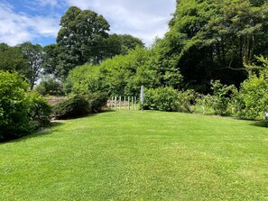 A well-maintained grassy area with a variety of trees and shrubs, a stone wall, and a metal fence. - Fabulous open plan house in country estate - 4 bedrooms, each with its own bathroom (By Arbroath)