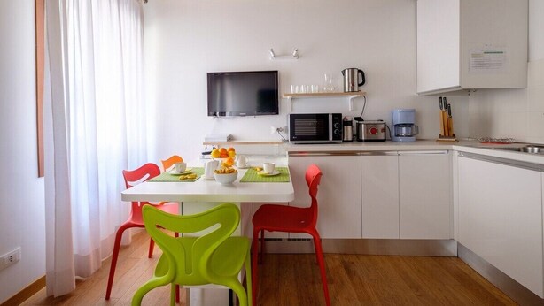 A compact kitchen with white cabinets, a microwave, a coffee maker, and a TV mounted above the counter. - Lion's 1 (Venice)