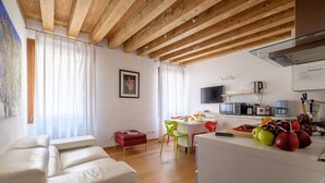 A modern living room with a sofa, a dining area with chairs, a kitchen with appliances, and a television. - Lion's 1 (Venice)