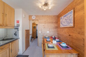 Cuina amb armaris de fusta, un rentaplat i zona de menjador amb taula per a dues persones.